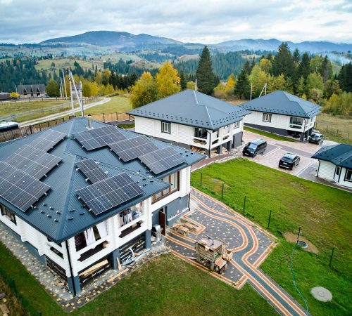 Aerial view of new modern house cottage in the mountains with solar photovoltaic panel system on roof. Concept of alternative, renewable energy and home autonomy.